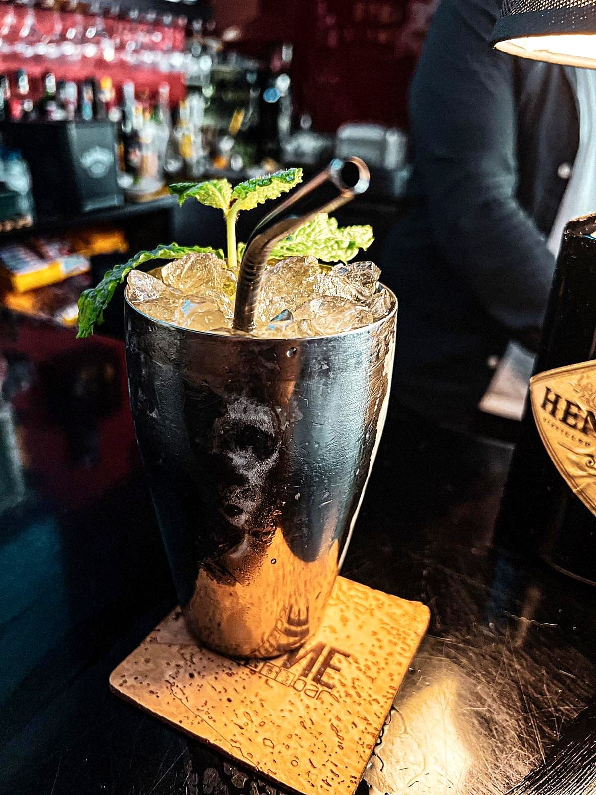 Cocktail com gelo picado e hortelã num copo metálico com caveira, sobre base de cortiça IKONE