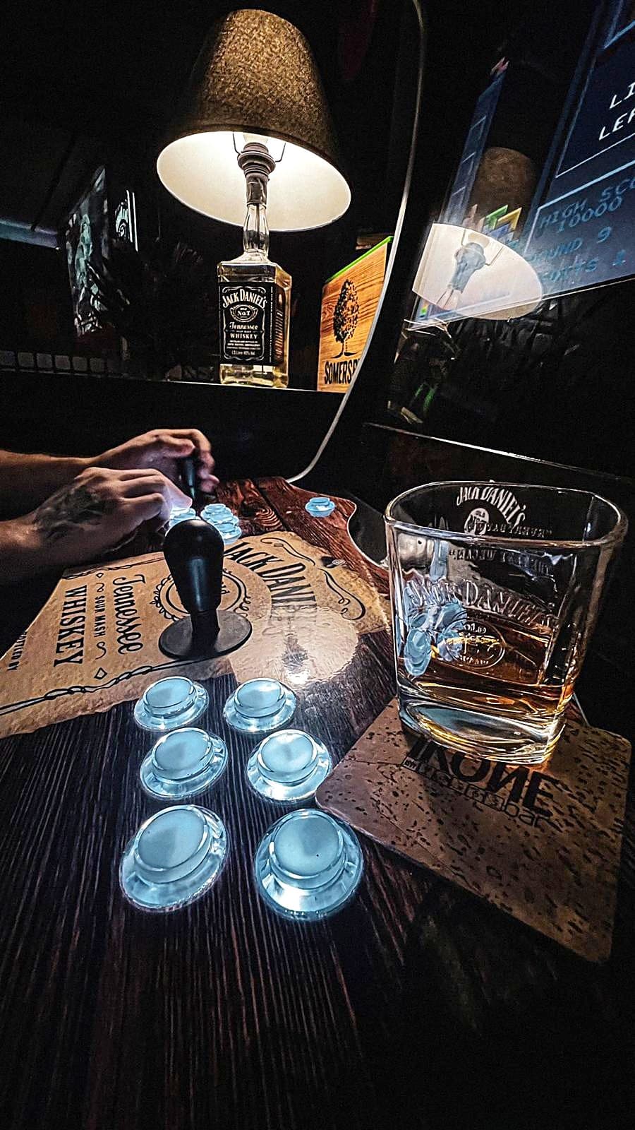 Comandos de máquina arcade iluminados ao lado de um copo de whisky com gelo