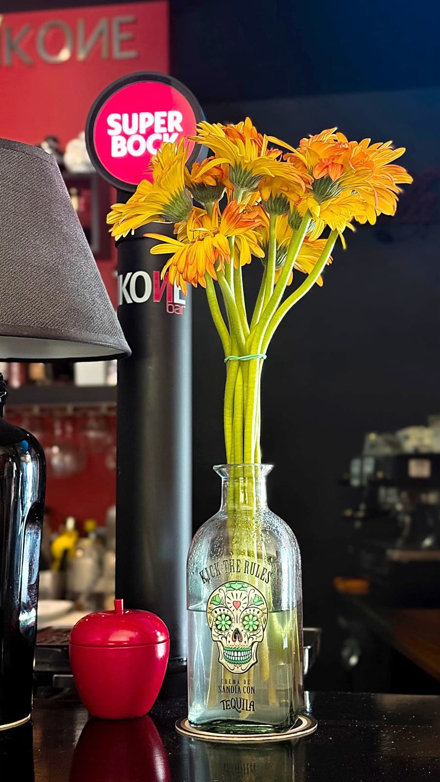Flores laranja numa garrafa decorada, com o letreiro IKONE ao fundo