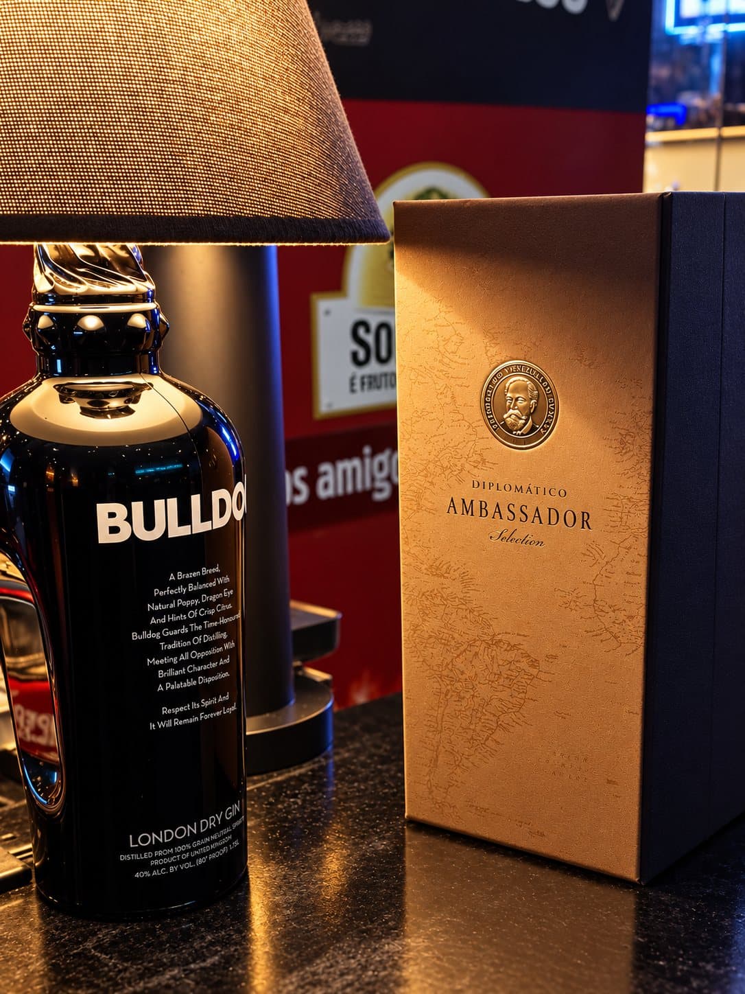 Garrafa de gin Bulldog ao lado da caixa do rum Diplomático Ambassador, sob um candeeiro